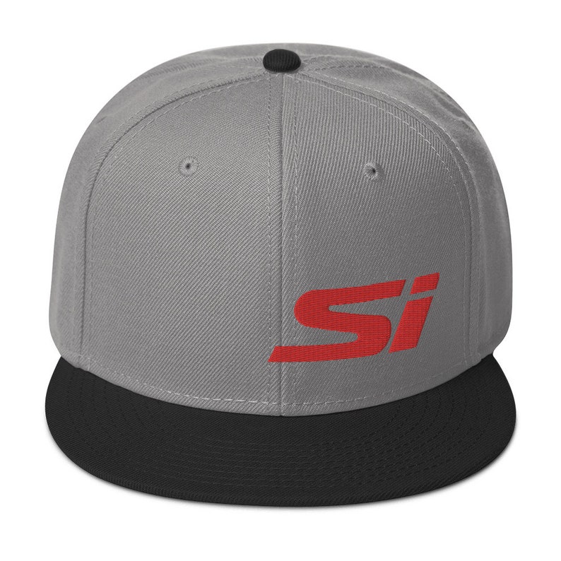 May include: A gray flat-brimmed baseball cap with a black brim and a red "SI" logo on the front. The cap has a structured fit and a button on top. This hat is a stylish accessory.