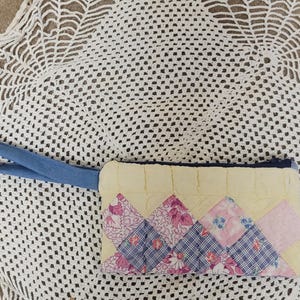 May include: A quilted clutch with a light yellow background and a geometric pattern of pink and blue floral fabric. It has a blue denim handle and a dark blue zipper.