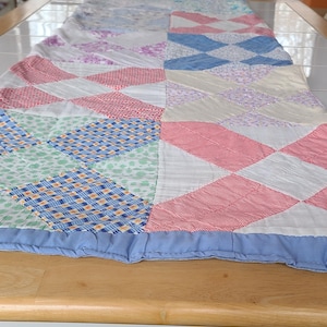 May include: A colorful patchwork quilt with a variety of patterns and colors, including red, blue, white, and green. The quilt has a blue border and is likely handmade. The quilt is a decorative textile.