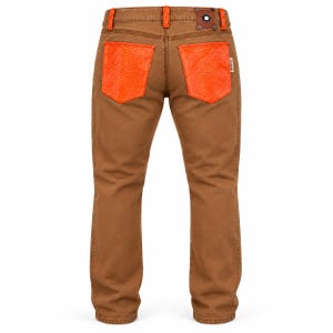 May include: Brown denim jeans featuring bright orange textured back pockets with a snakeskin-like pattern. The waistband includes orange belt loops and a dark brown leather-like patch with a central metal rivet detail on the back right side.