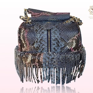 Peut inclure: Un sac à main en cuir de serpent bleu et rose avec une bordure en franges. Le sac a une fermeture éclair dorée et une bandoulière en chaîne.
