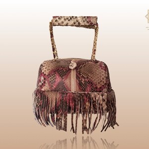 Peut inclure: Un petit sac à main en peau de serpent brun et rose avec une poignée en chaîne dorée et une bordure en franges.