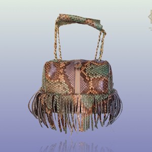 Peut inclure: Un petit sac à main en peau de serpent brun, vert et beige avec une bandoulière en chaîne dorée et une bordure en franges.