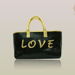 Peut inclure: Sac cabas en cuir noir avec des finitions dorées et le mot "LOVE" écrit en lettres dorées.