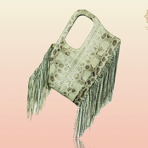 Peut inclure: Un sac à main en cuir de serpent blanc et brun avec une bordure en franges. Le sac a une poignée supérieure et une petite ouverture en haut.