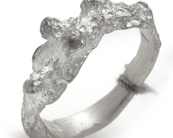 Puede incluir: Un anillo de plata con un diseño orgánico texturizado. El anillo está hecho de una sola pieza de metal y tiene una superficie rugosa y desigual.