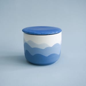 May include: A blue and white ceramic jar with a lid. The jar has a wavy design that resembles mountains or hills. The jar is perfect for storing small items like jewelry or trinkets.