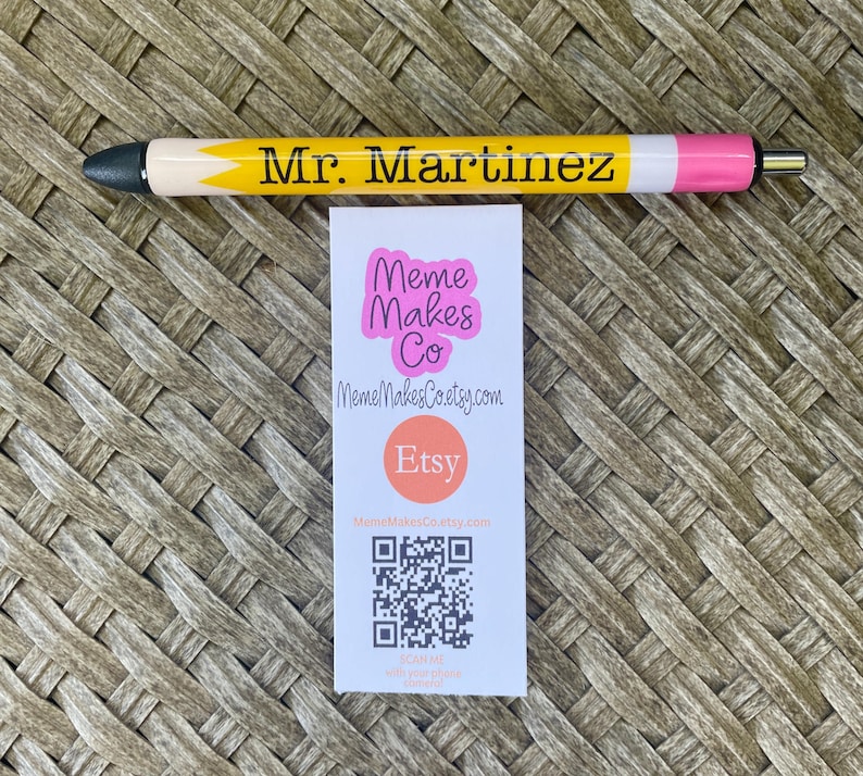 以下が含まれることがあります： ピンクの文字で「Meme Makes Co」と書かれた白い名刺。名刺には「MemeMakesCoetsy.com」というウェブサイト、赤い円の中に「Etsy」という単語、QRコードも記載されています。
