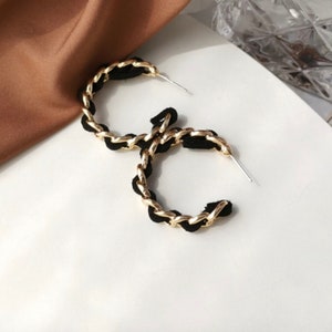 May include: A pair of gold and black hoop earrings. The hoops are made of a thick chain with a black fabric covering.