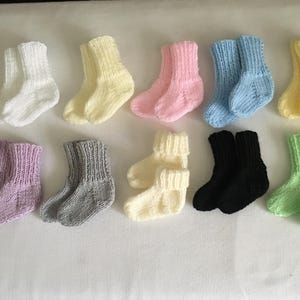 May include: A collection of ten pairs of knitted baby socks in various colors, including white, yellow, pink, light blue, lavender, gray, cream, black, and light green. The socks are arranged on a white surface.