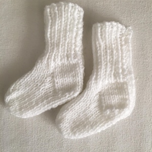 May include: A pair of small, knitted white socks. The socks are made of a soft, textured yarn and have a ribbed cuff. The socks are designed for a baby or small child.