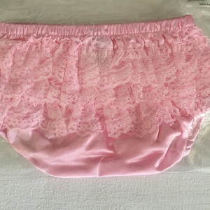 May include: Pink ruffled baby bloomers made of 100% polyester. The bloomers have a satin-like finish and are decorated with a layer of delicate lace.