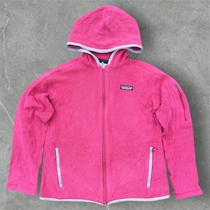 May include: A bright pink fleece zip-up hoodie featuring a full-length front zip, a hood with light grey trim, two vertical zipped hand pockets, and a small zipped pocket on the left sleeve. A Patagonia brand logo patch is on the chest.