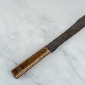 Könnte beinhalten: Ein vintage, rostiges, Metallmesser mit einem Holzgriff. Das Messer hat einen Messingniet am Griff.