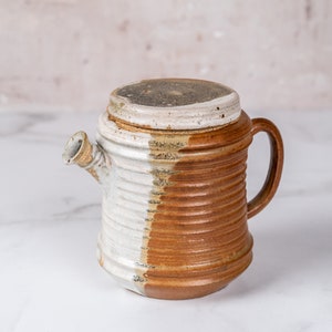 May include: A brown and white ceramic teapot with a lid and a handle. The teapot has a textured, ribbed design.