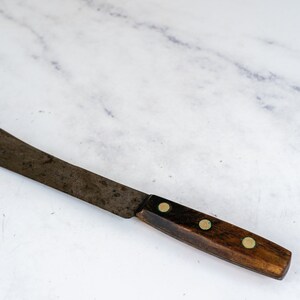 May include: A vintage kitchen knife with a wooden handle and brass rivets. The blade is rusty and has a curved shape.