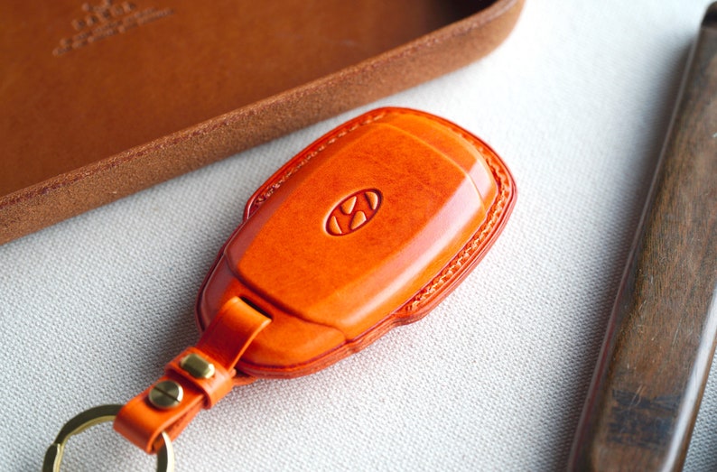 May include: Orange leather key fob with a metal key ring and the Hyundai logo embossed on the front.