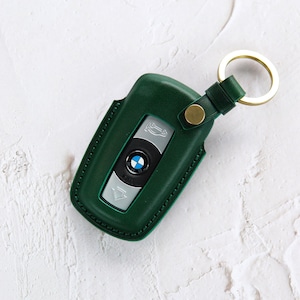 Puede incluir: Un llavero de cuero verde con un anillo de llave dorado y un logotipo BMW plateado.