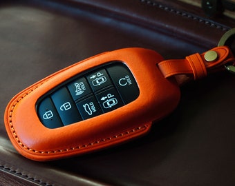 May include: Orange leather key fob with a black keyless entry remote. The remote has buttons for lock, unlock, trunk, panic, and hold.
