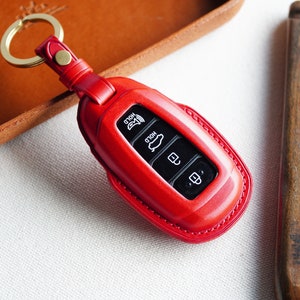May include: Red leather key fob with a gold key ring. The fob has four buttons with icons for "Hold", "Hold", "Unlock", and "Lock".