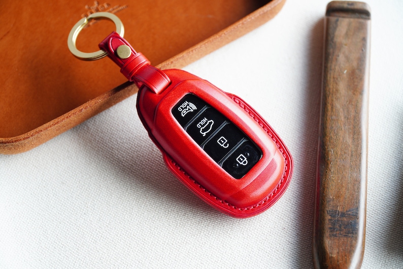 May include: Red leather key fob with a gold key ring. The fob has four buttons with icons for "Hold", "Hold", "Unlock", and "Lock".