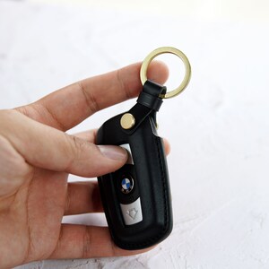 Puede incluir: Llavero de cuero negro con un anillo de llave dorado y un logotipo BMW plateado.
