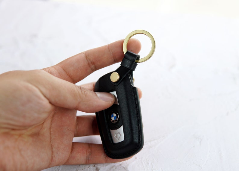 Puede incluir: Llavero de cuero negro con un anillo de llave dorado y un logotipo BMW plateado.