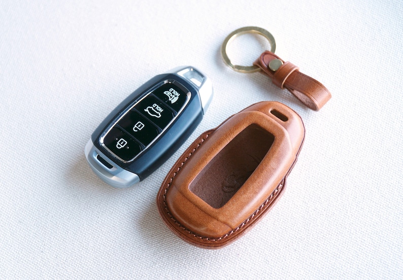 May include: A brown leather key fob with a silver key inside. The key fob has a key ring attached to it.