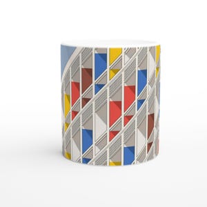 Peut inclure: Mug en céramique blanche avec un motif géométrique coloré de carrés et de rectangles bleus, rouges, jaunes et bruns. Le motif ressemble à une façade de bâtiment.