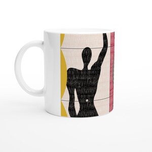 May include: White ceramic mug featuring a black silhouette of a person against a background of yellow, red, and white geometric shapes.