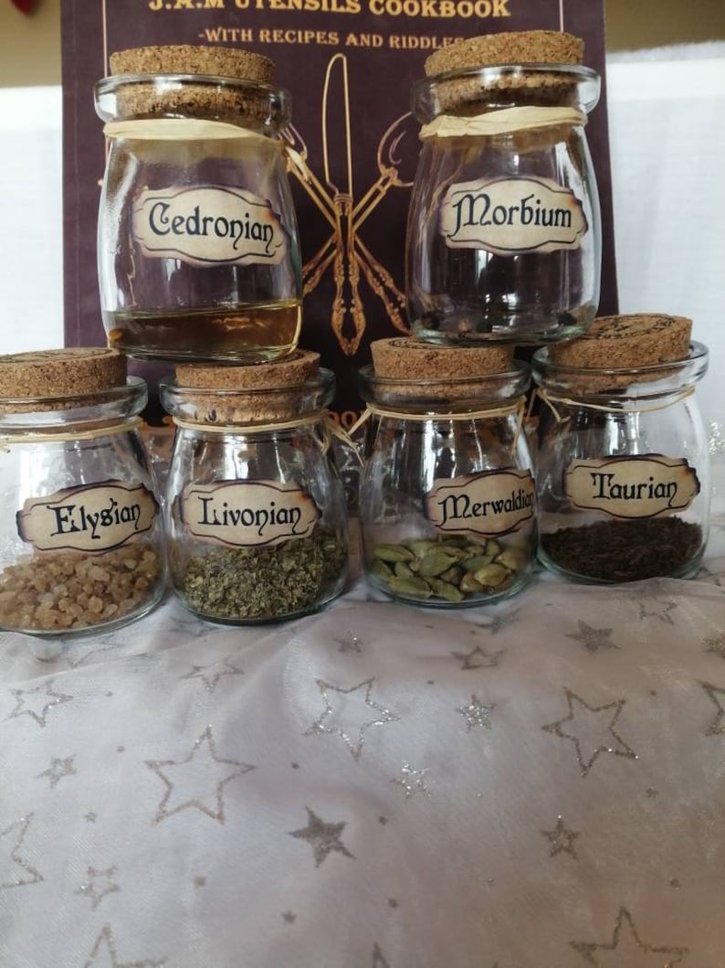 May include: Six small glass jars with cork lids, each containing different ingredients. The jars are labeled with handwritten labels: "Cedronian", "Morbium", "Elysian", "Livonian", "Merwalkin", and "Taurian".