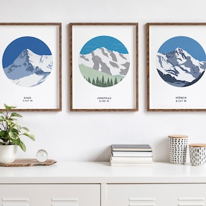 May include: Three framed prints of mountain landscapes with blue skies and snow-capped peaks. The prints are labeled "Eiger 3,967 M", "Jungfrau 4,158 M", and "Mönch 4,107 M".