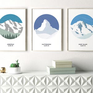May include: Three framed prints of mountain silhouettes with blue backgrounds and white snow. The prints are labeled "Jungfrau 4,158 m", "Matterhorn 4,478 m", and "Mont Blanc 4,809 m".