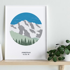 May include: A white framed print with a blue, green, and gray illustration of a mountain range in a circle. The text "JUNGFRAU 4,158 M" is below the illustration.