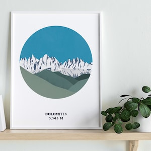 May include: A white framed print with a blue circle depicting a snowy mountain range with green hills in the foreground. The text "Dolomites 3,343 M" is printed below the circle.