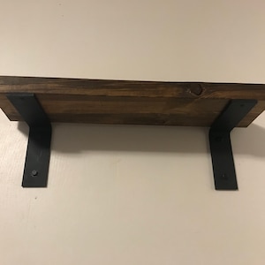 May include: A wooden shelf with black metal brackets. The shelf is stained a dark brown color and the brackets are a matte black.
