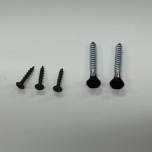May include: An assortment of screws, including three black screws and two silver screws with black heads. The screws are arranged on a white surface, showcasing their different sizes and designs. Ideal for various construction and repair projects.