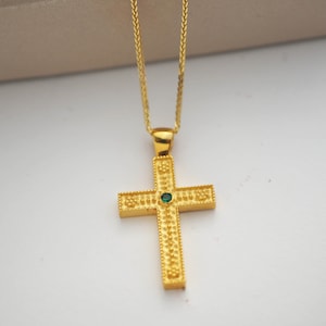 Peut inclure: Un collier en chaîne dorée avec un pendentif en forme de croix dorée orné d'une pierre précieuse verte au centre.
