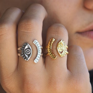May include: Two gold and silver rings featuring an eye design. The rings are worn on the index and middle fingers of a person's hand.