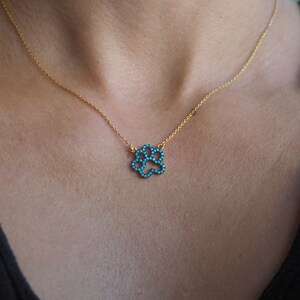 Op de afbeelding: Een gouden ketting met een turquoise hondenpoot hanger.