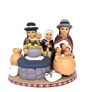 May include: A ceramic figurine set depicting a family scene with two adults wearing hats, one carrying a baby, and a child standing between them. They are positioned around a stone grinding table, clay pots, and a white cloth on an oval base.