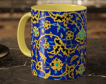 May include: A ceramic mug with a yellow handle and interior. The exterior features a blue background with a gold floral pattern and turquoise accents. The mug is sitting on a dark countertop.