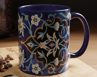 May include: A blue ceramic mug with a colorful floral pattern. The mug has a black background with intricate details in blue, green, and white. The mug is sitting on a wooden surface.