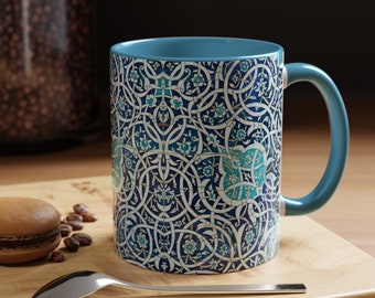 May include: A blue ceramic mug with a white and blue intricate floral pattern. The mug has a handle and is sitting on a wooden surface.