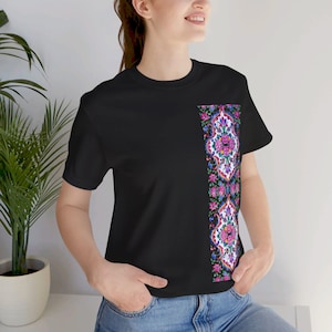 Puede incluir: Camiseta negra con un patrón floral vertical en el lado derecho. El patrón presenta flores rosas, azules y blancas, así como diseños geométricos.