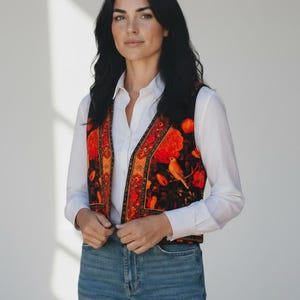 Könnte beinhalten: Eine farbenfrohe Weste mit Blumen- und Vogelmuster. Die Weste hat einen schwarzen Hintergrund mit orangefarbenen und roten Blumen und einem Vogel. Die Weste wird über einem weißen Hemd und einer blauen Jeans getragen.