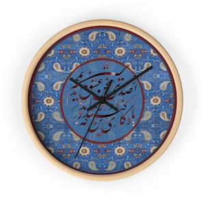 Puede incluir: Un reloj de pared con estampado azul y blanco con marco de madera. La esfera del reloj presenta caligrafía árabe en rojo y negro.