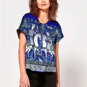 Op de afbeelding: Een blauw en wit gepatroneerd shirt met korte mouwen met een ontwerp van mensen die op paarden rijden. Het shirt heeft een ronde hals en een ontspannen pasvorm.