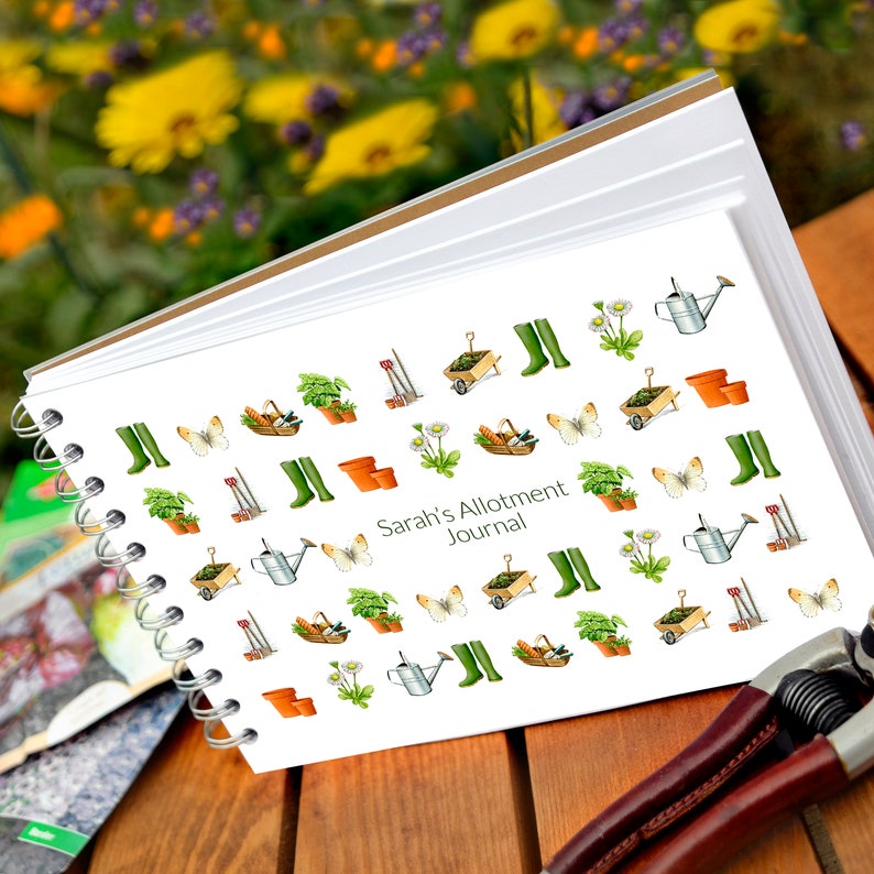 May include: A white spiral bound journal with a green and brown gardening themed design. The cover features a variety of gardening tools, plants, and butterflies. The text "Sarah's Allotment Journal" is printed in black on the front cover.