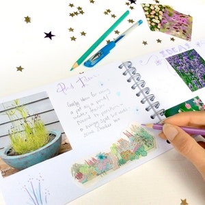 May include: A notebook with a handwritten note about a water feature idea for a garden. The note says "lovely idea for using a pot as a pond! water feature. Need to position in a sunny spot but needs some shade hoo". The notebook has a spiral binding and is open to a page with a photo of a small pond and a drawing of a garden.